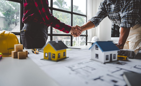 two people shaking hands over building plans.
